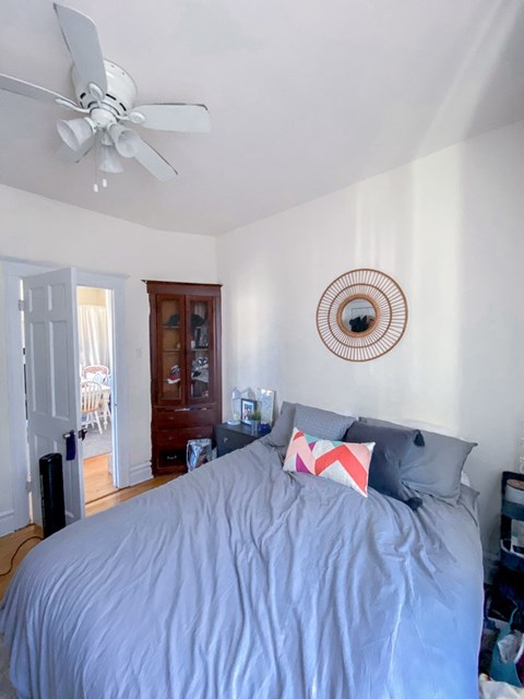 A bedroom with a bed, a ceiling fan, and a mirror on the wall.