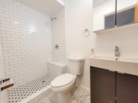 A white toilet in a bathroom with a white tiled shower.