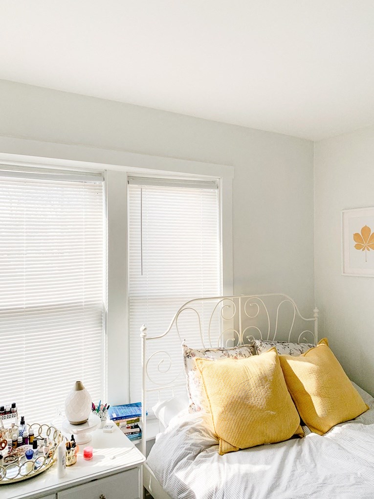 a bedroom with a bed with yellow pillows next to two windows