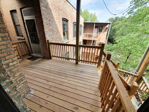 A wooden deck with a railing and a brick building in the background.