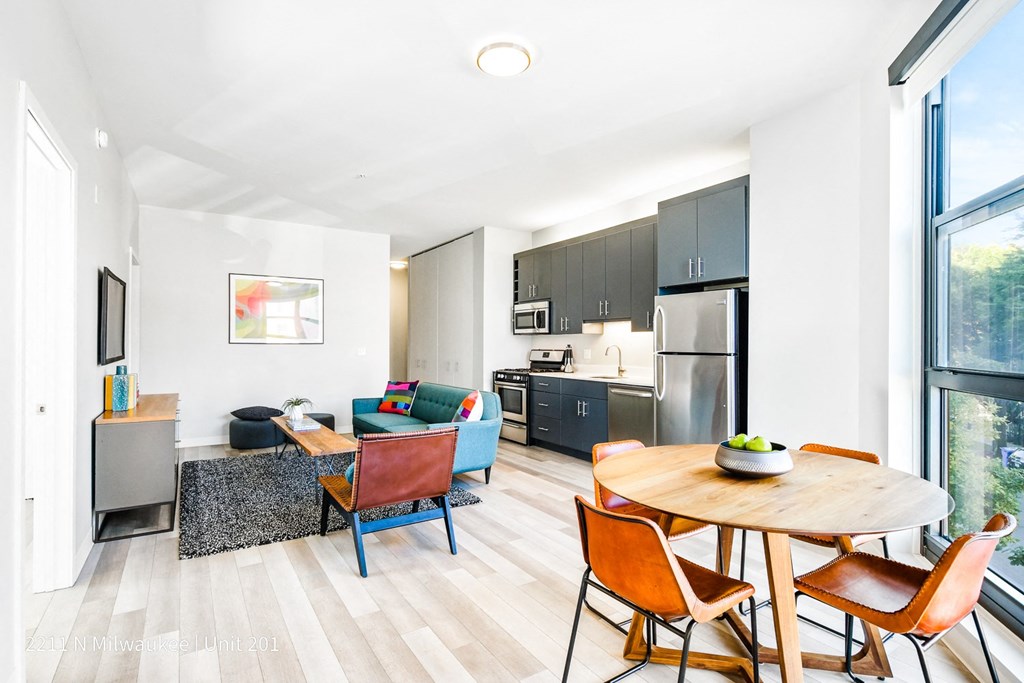 Stylish round wooden table and chairs set positioned in front of the open-concept living room and kitchen at L Logan Square Apartments.