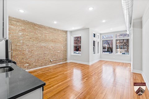 A spacious living room with a brick wall and hardwood floors.