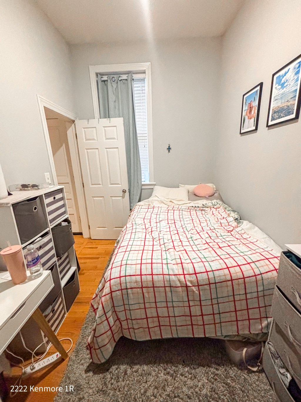 A bedroom with a bed, a desk, and a window with a curtain.
