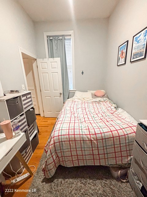 A bedroom with a bed, a desk, and a window with a curtain.