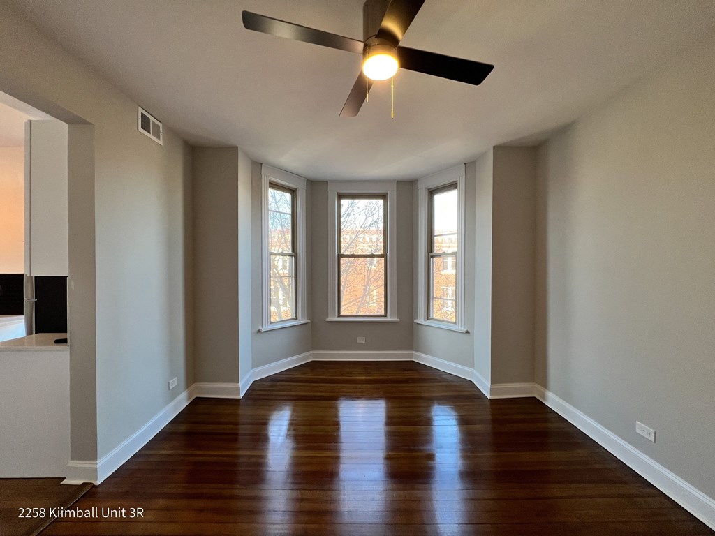 A room with a ceiling fan and three windows.