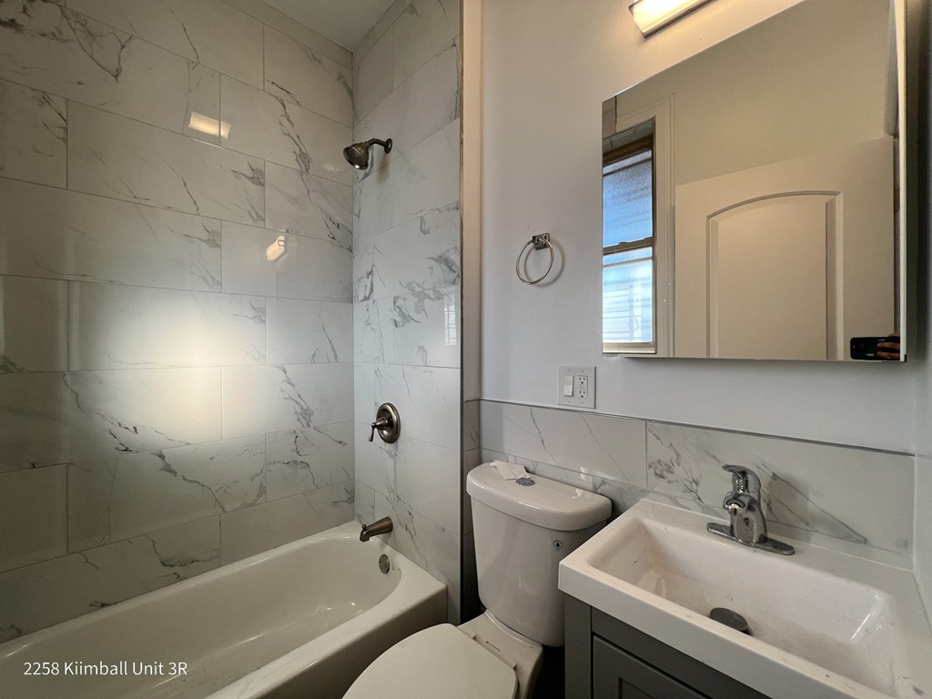 A white bathroom with a marble tile wall and a tub, toilet, and sink.