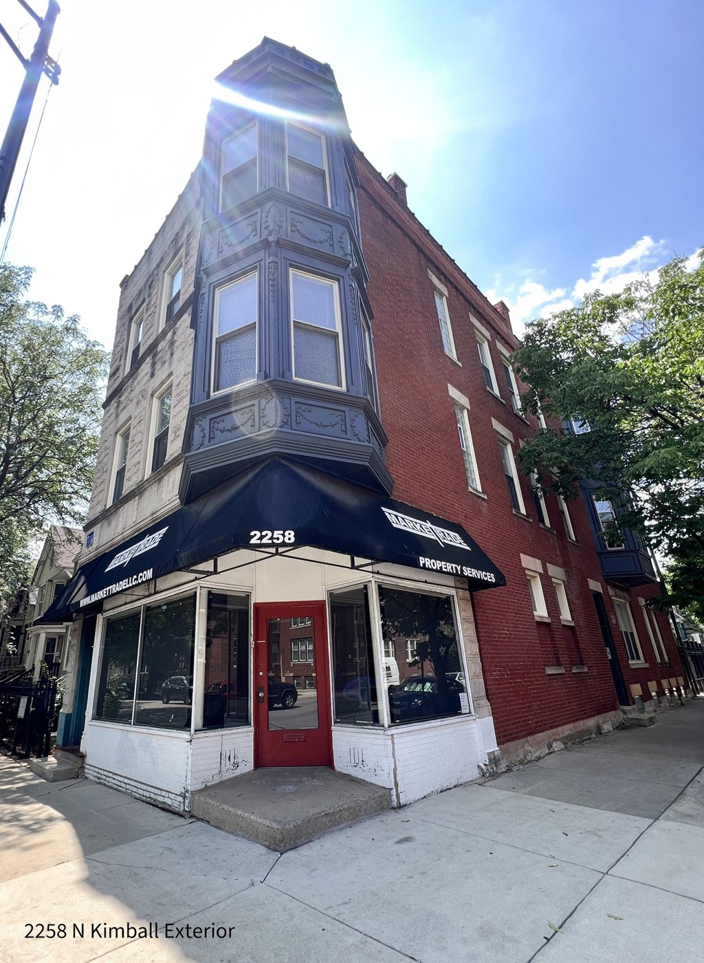 a building on the corner of a street with a red door and a black awning