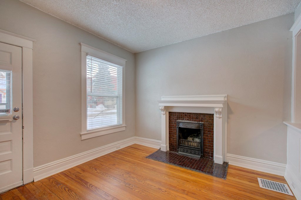 an empty living room with a brick fireplace and wooden floors