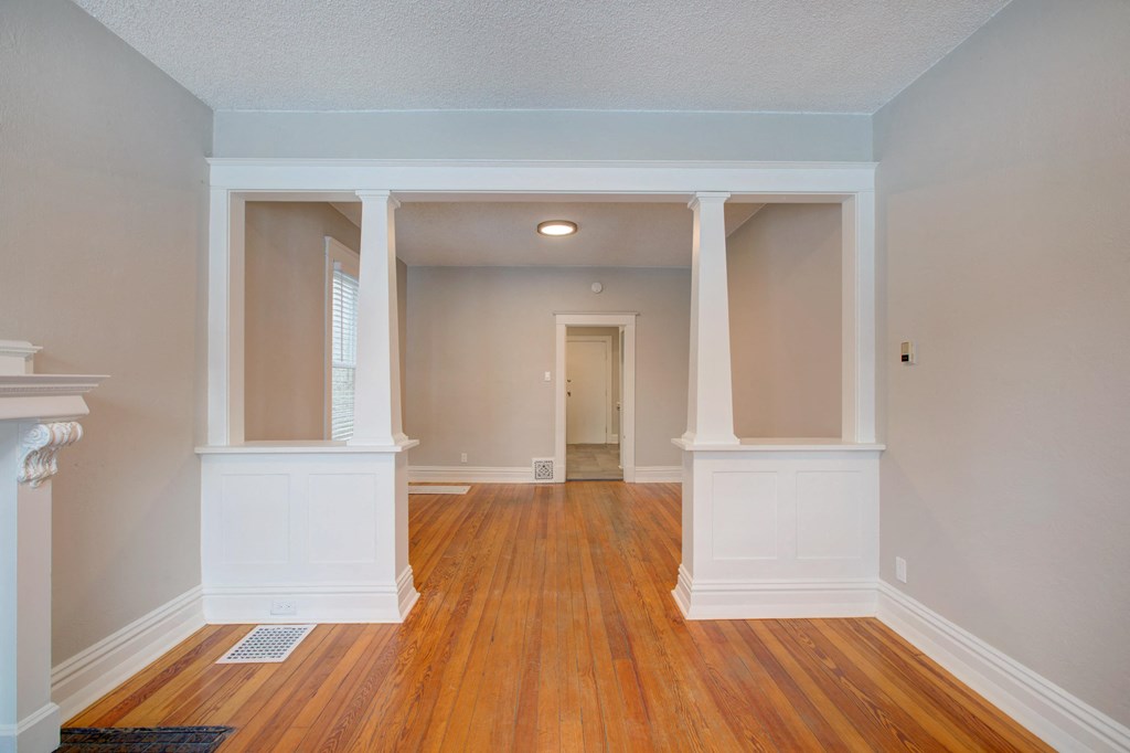 an empty living room with white pillars and wood floors
