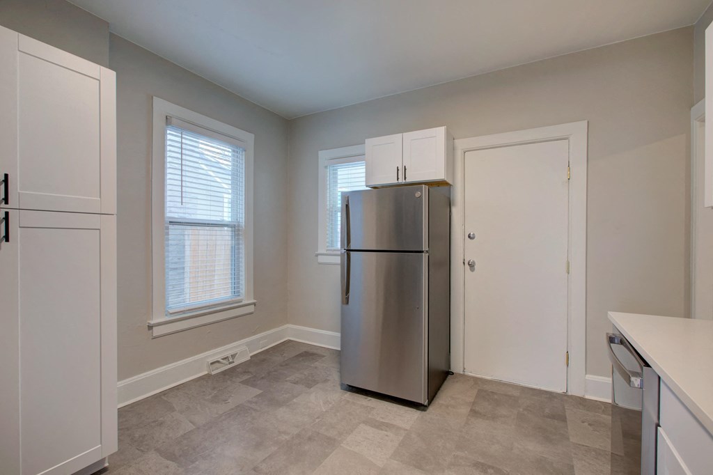 an empty kitchen with a stainless steel refrigerator and white cabinets