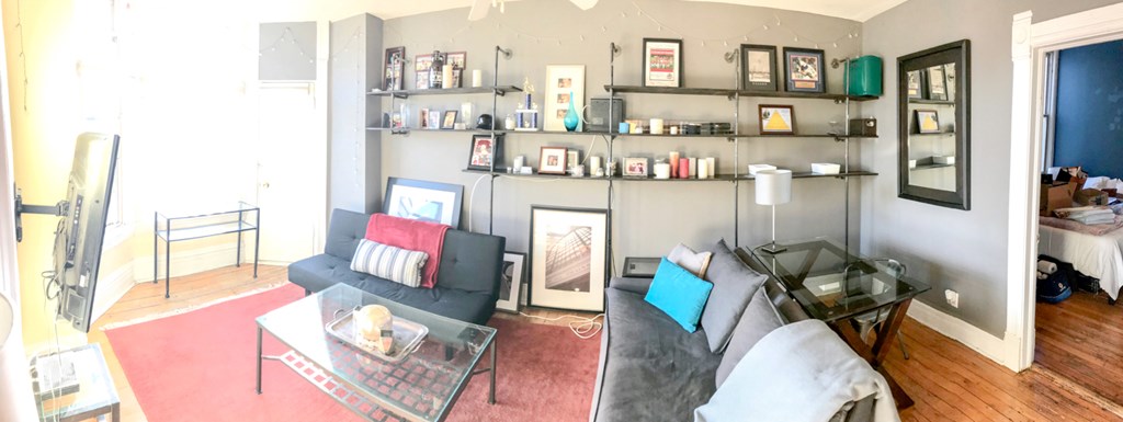 A living room with a glass coffee table and a grey couch.