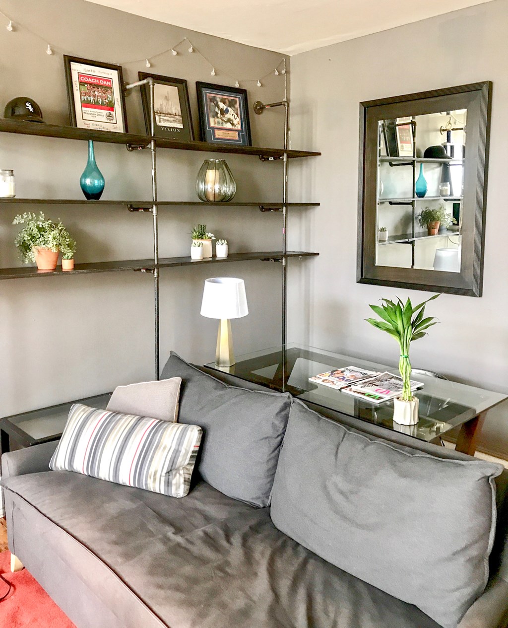 A grey couch with a striped pillow and a glass table with a plant on it.