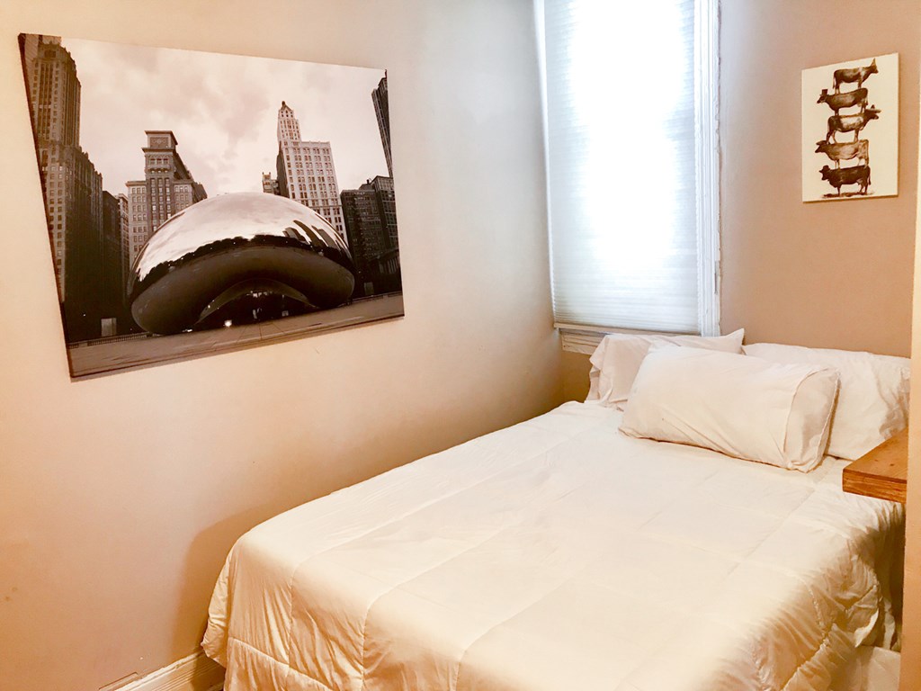 A bedroom with a white bed and a picture of a city skyline on the wall.