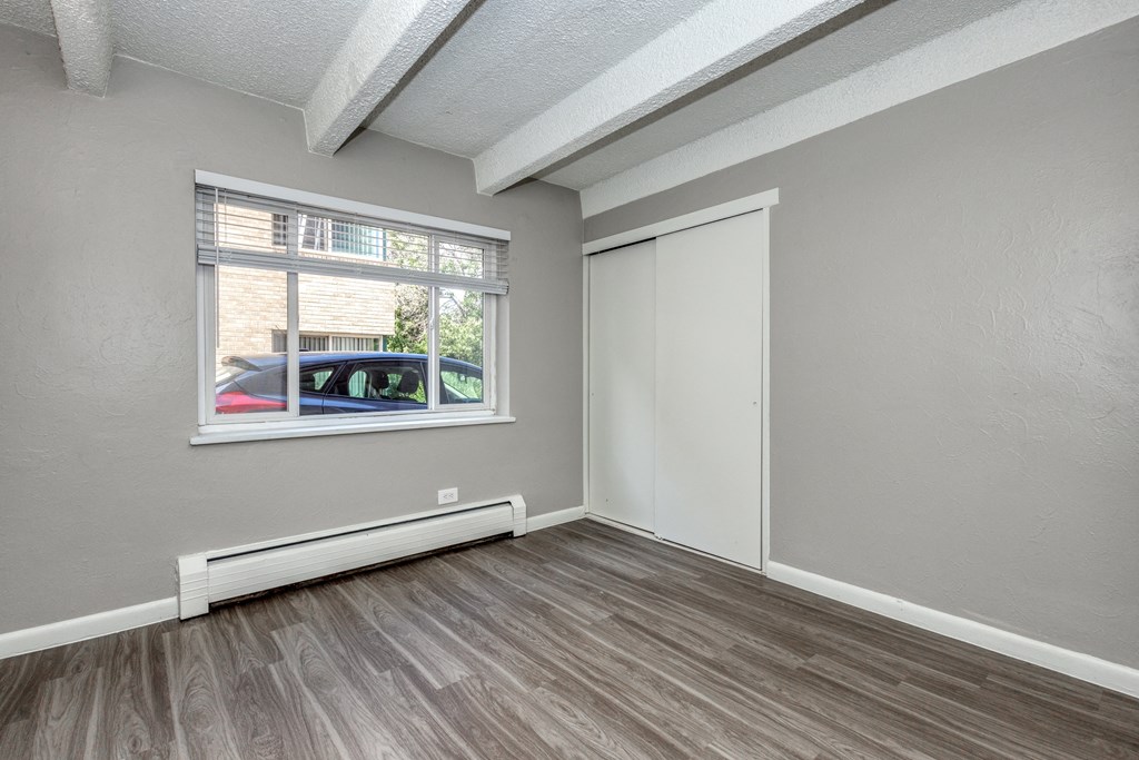 an empty bedroom with a window and wood flooring