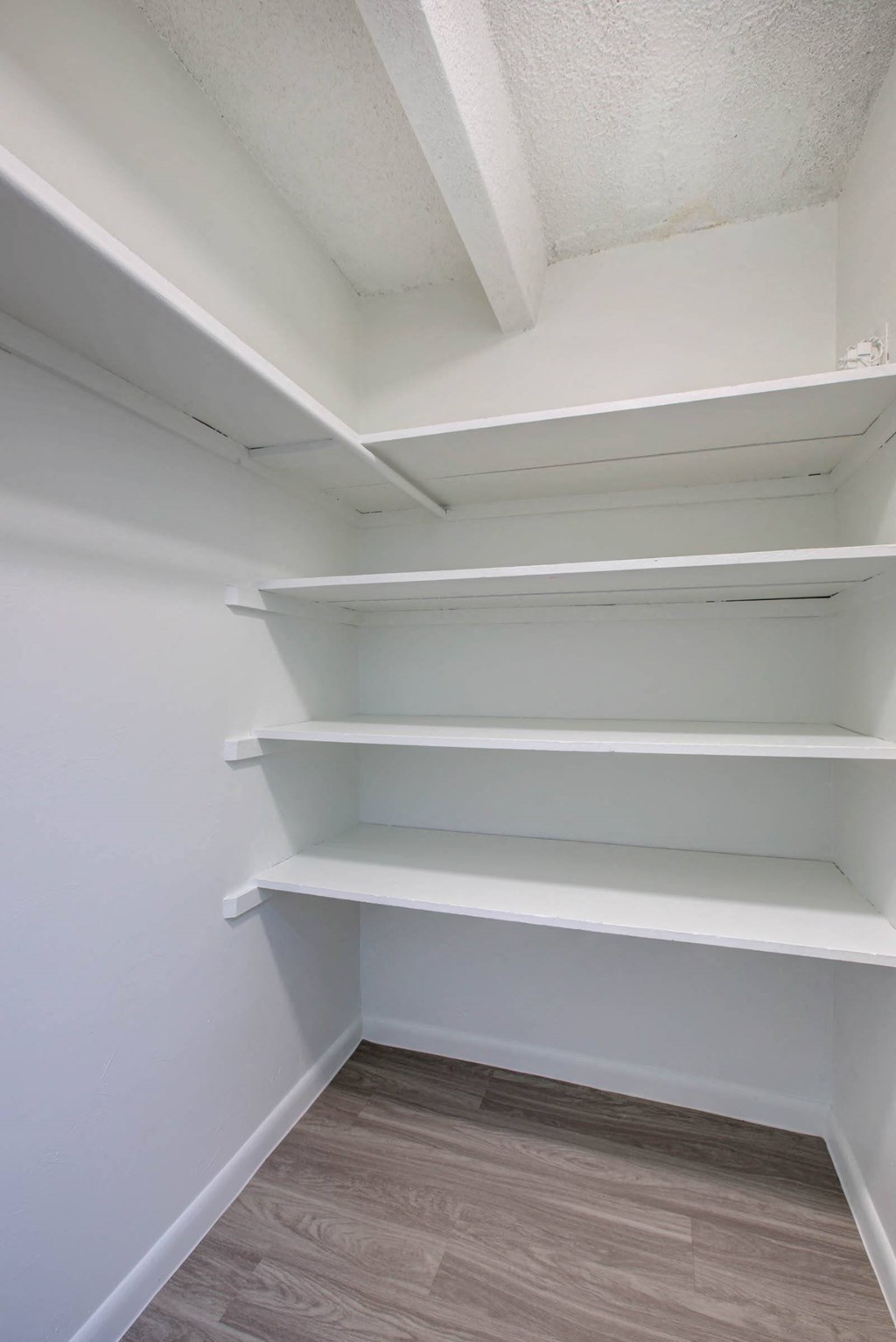 a walk in closet with white shelves and a wood floor