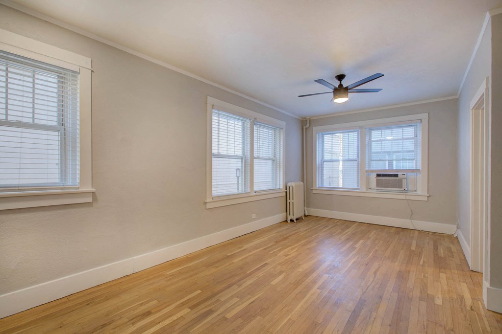 an empty living room with a ceiling fan and three windows