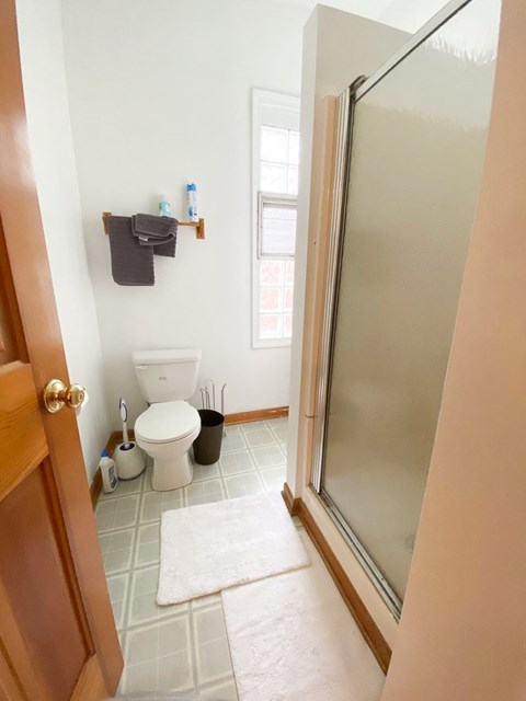 A bathroom with a toilet, a trash can, a towel rack, and a rug.