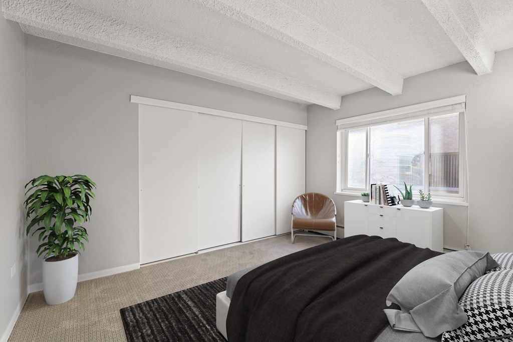 A bedroom with a bed, chair, and potted plant.