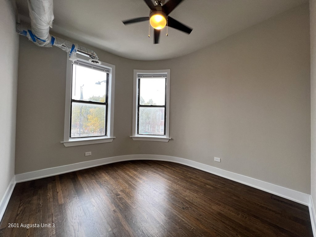 an empty living room with a ceiling fan and two windows