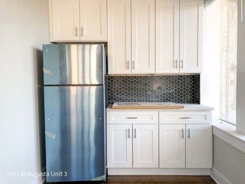 A kitchen with a stainless steel refrigerator and white cabinets.