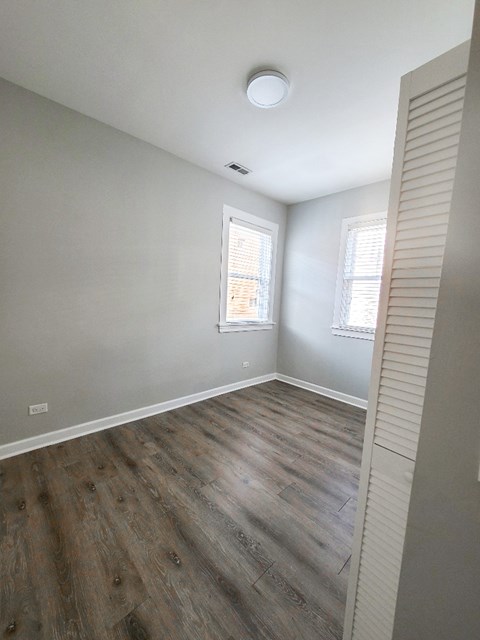 A room with wooden flooring and two windows.