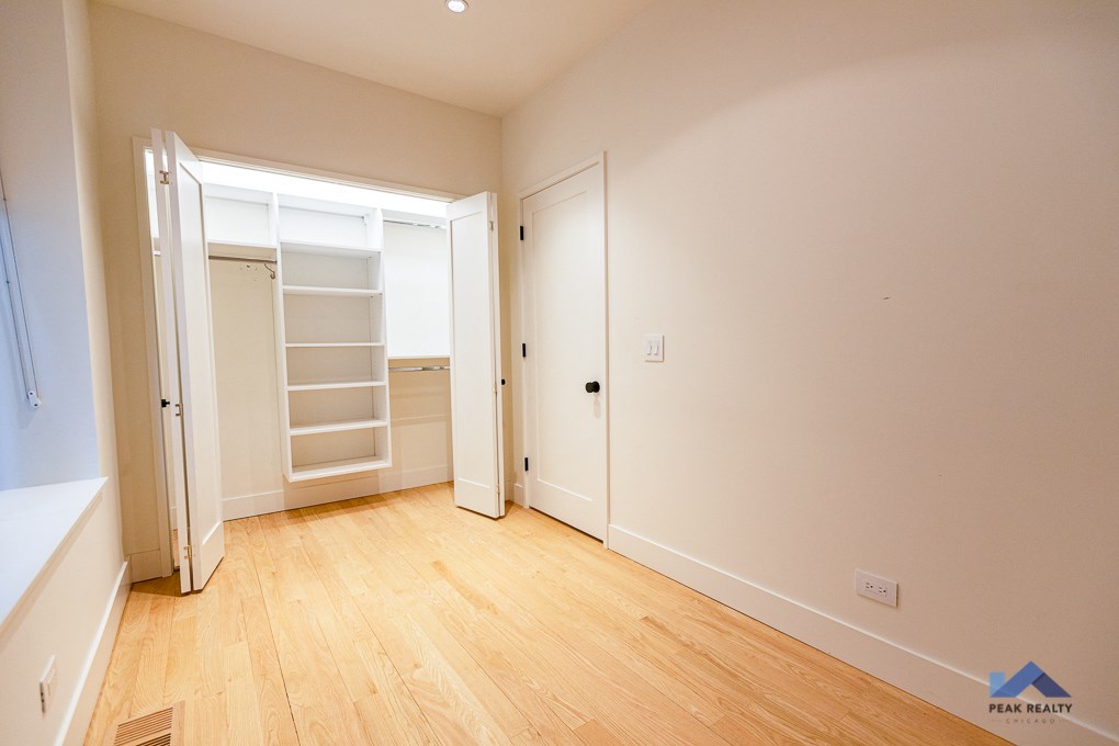 a bedroom with white walls and wood floors and a closet