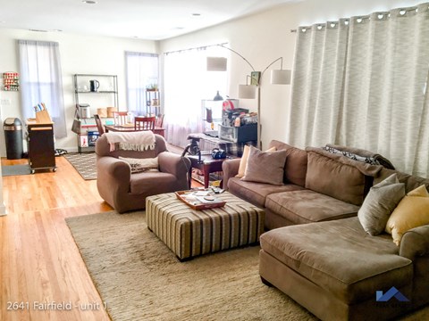 A living room with brown furniture and a striped ottoman.
