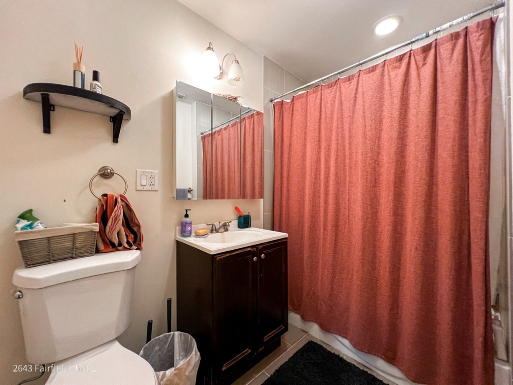 a bathroom with a shower toilet and sink and a red shower curtain