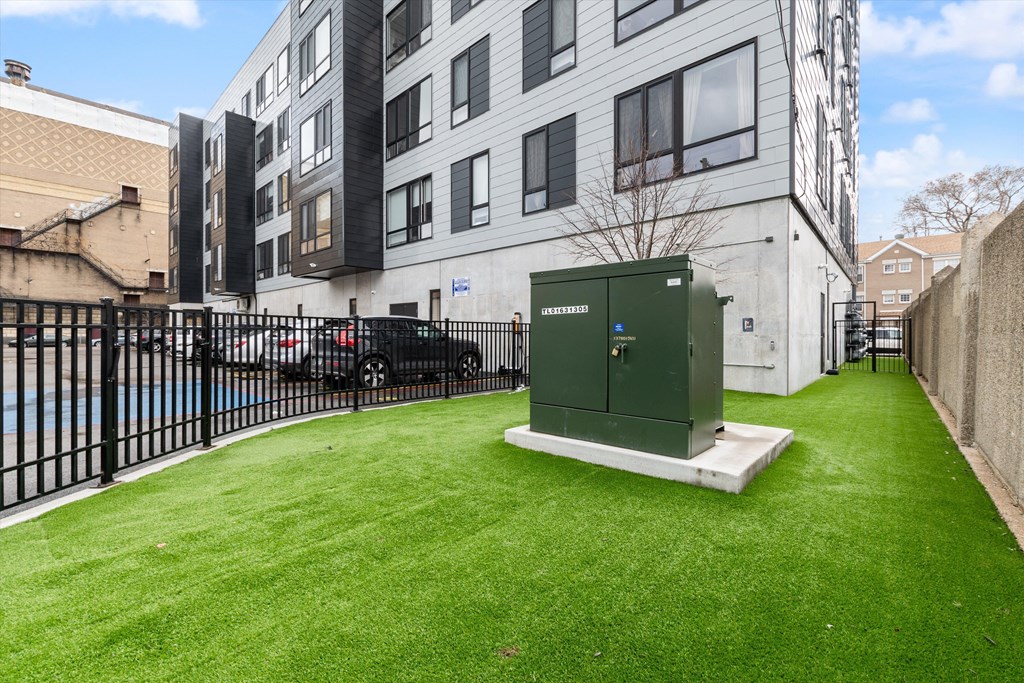 a green utility box sits in the middle of a grassy area in front of a building