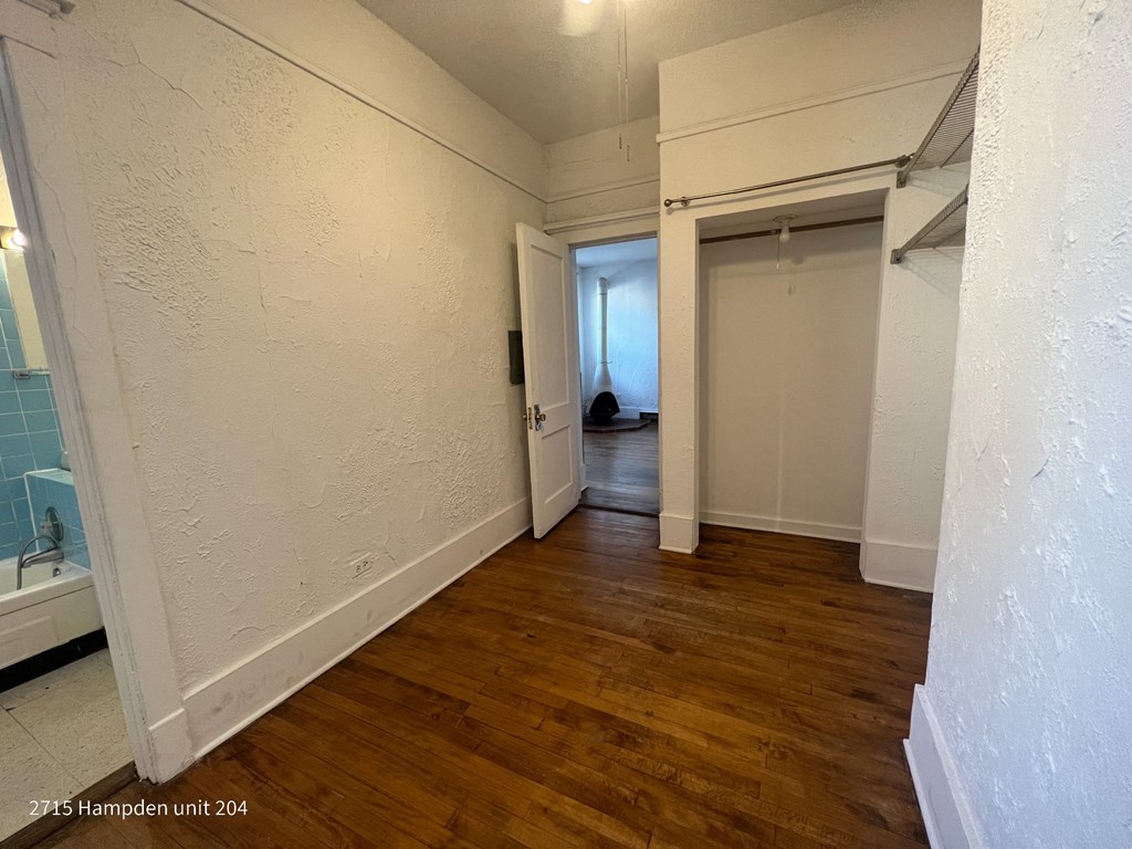 A room with wooden floors and white walls, with a doorway leading to another room.