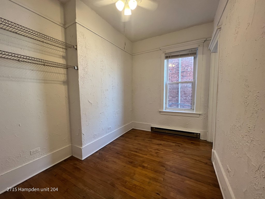 A room with wooden floors and a window with a view of a brick building outside.