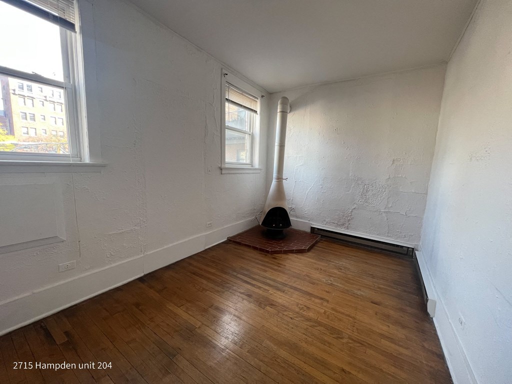 A room with wooden floors and white walls, with a window and a pipe running along the wall.