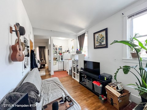A living room with a couch, a television, and a guitar hanging on the wall.