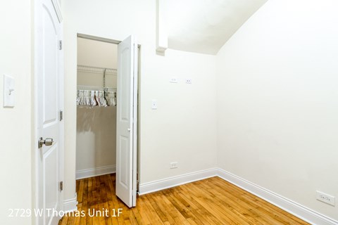 a bedroom with white walls and wood floors and a closet