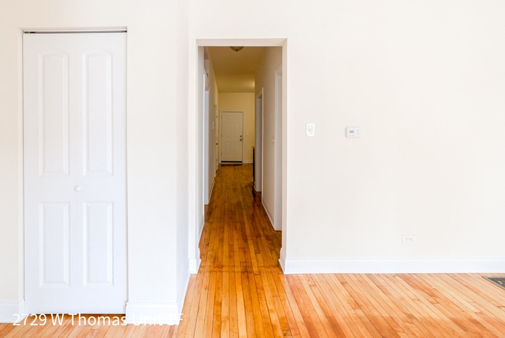 an empty hallway with wood floors and white walls and a door