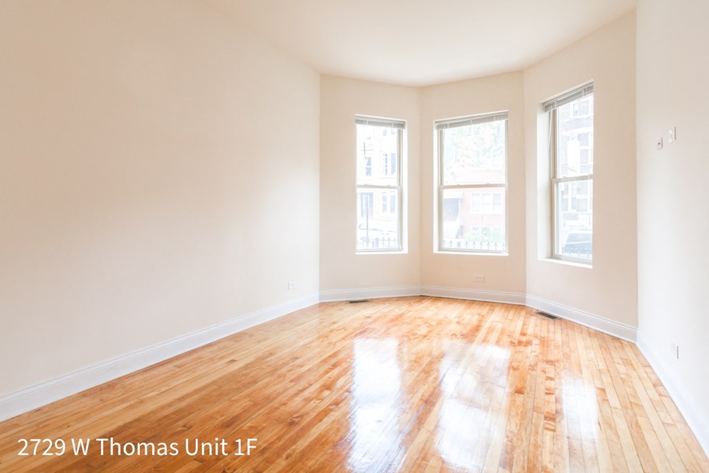 an empty room with wood floors and three windows