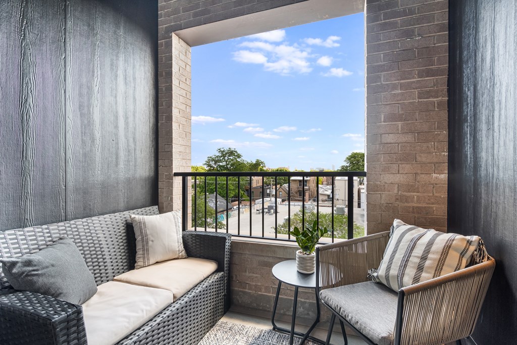 A balcony with a couch, chair, and table with a view of the street.