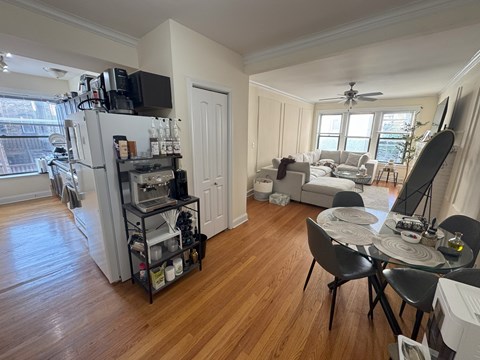 A kitchen with a refrigerator, a dining table with chairs, and a living room with a couch.