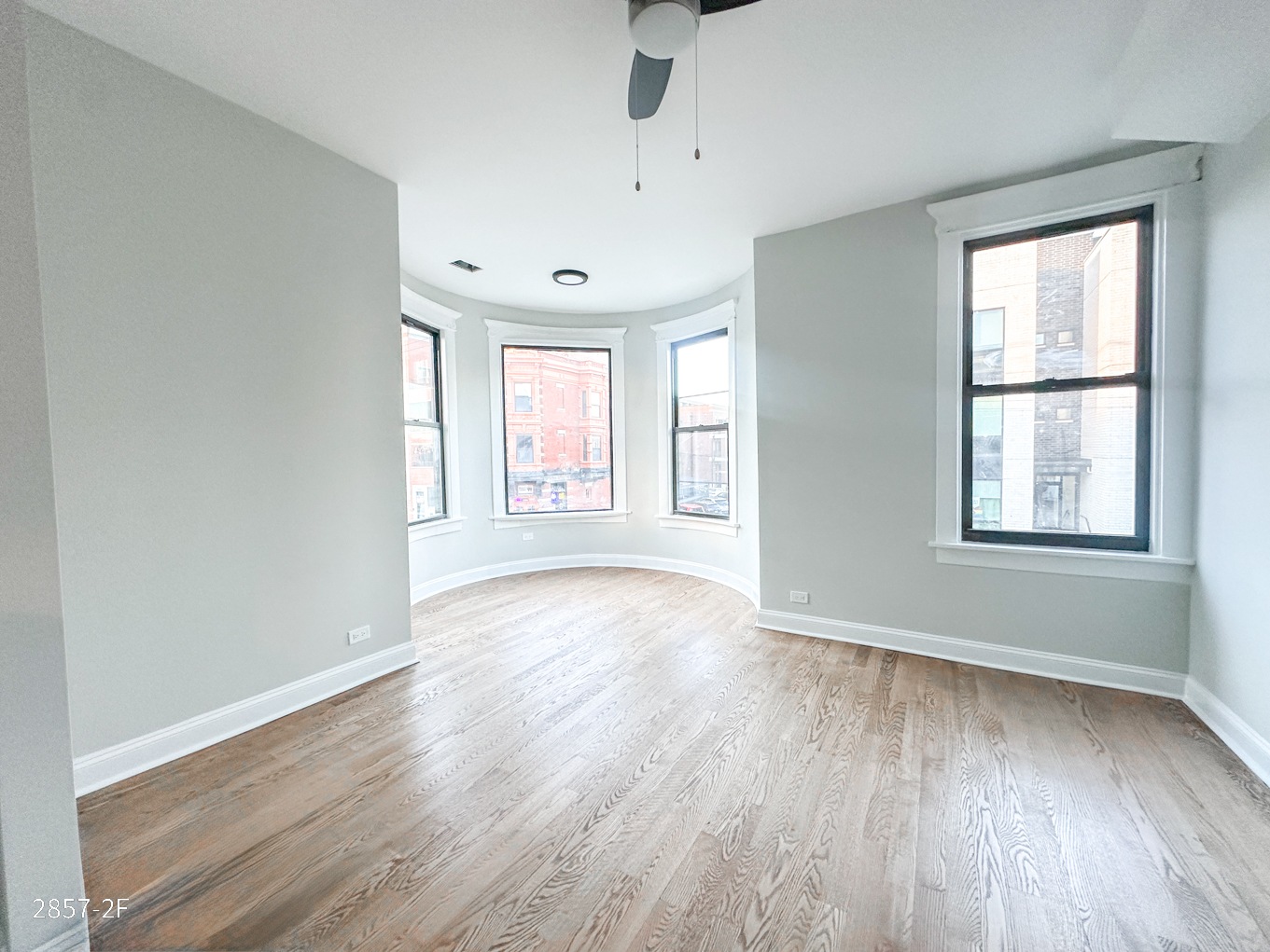 A spacious room with wooden floors and a ceiling fan.