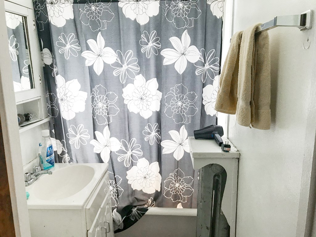 A bathroom with a white sink, a towel hanging on the wall, and a shower curtain with a floral pattern.