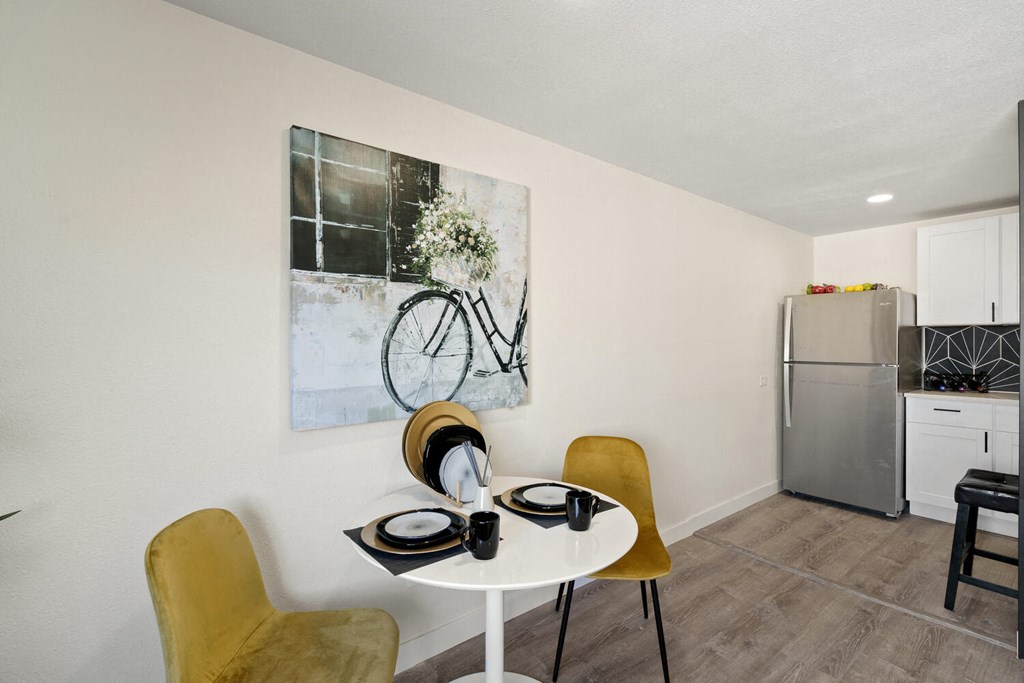 a dining area with a small table and two chairs and a kitchen in the background