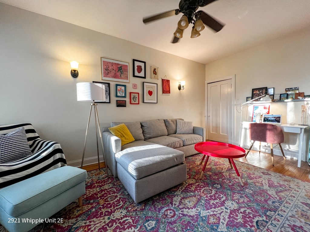 A living room with a grey couch, a red table, and a striped ottoman.