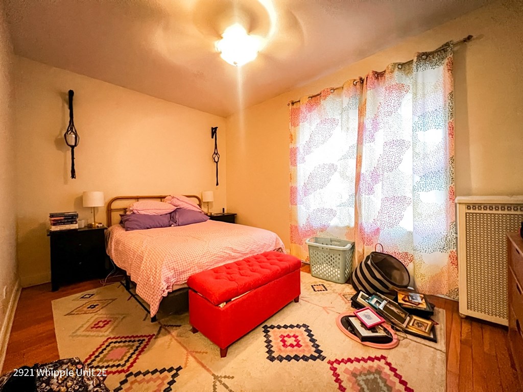 A bedroom with a bed, a red ottoman, and a rug with a geometric pattern.