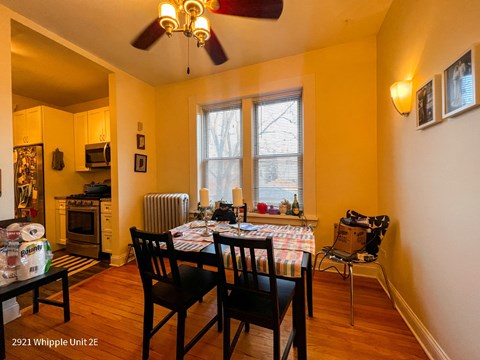 A dining room with a table set for two and a fan on the ceiling.