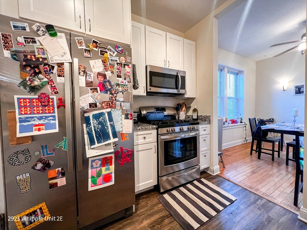 A kitchen with a refrigerator covered in magnets and a striped rug on the floor.