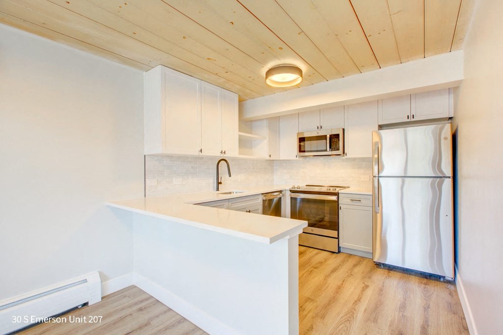 a small kitchen with white cabinets and a wooden ceiling