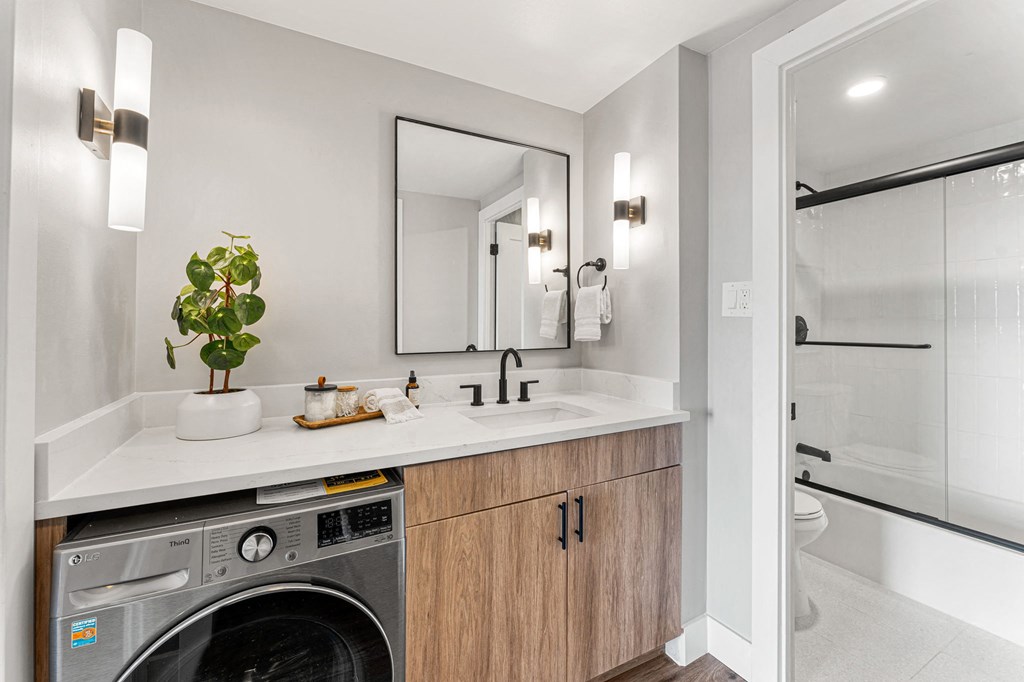 a bathroom with a sink, glass shower with tub, and an in-unit washing machine