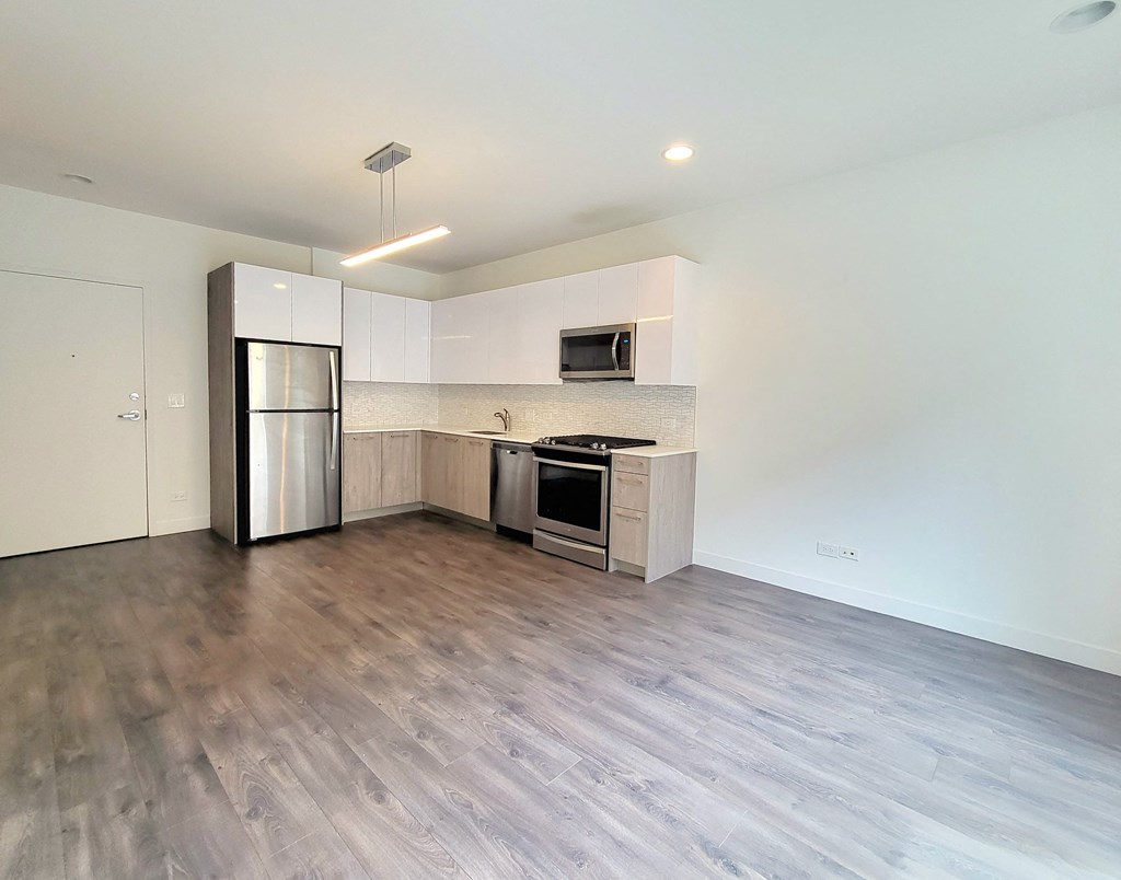 an empty living room with a kitchen with stainless steel appliances