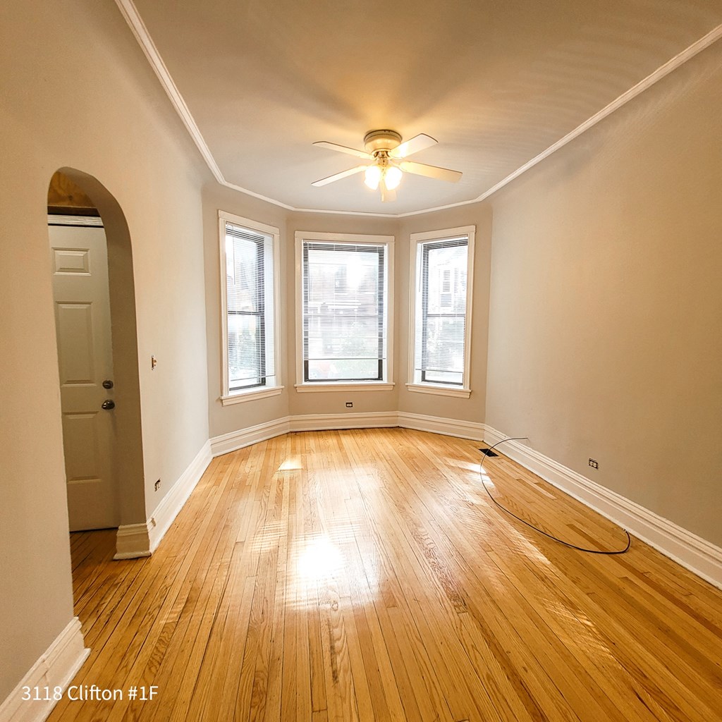 an empty living room with a ceiling fan and three windows