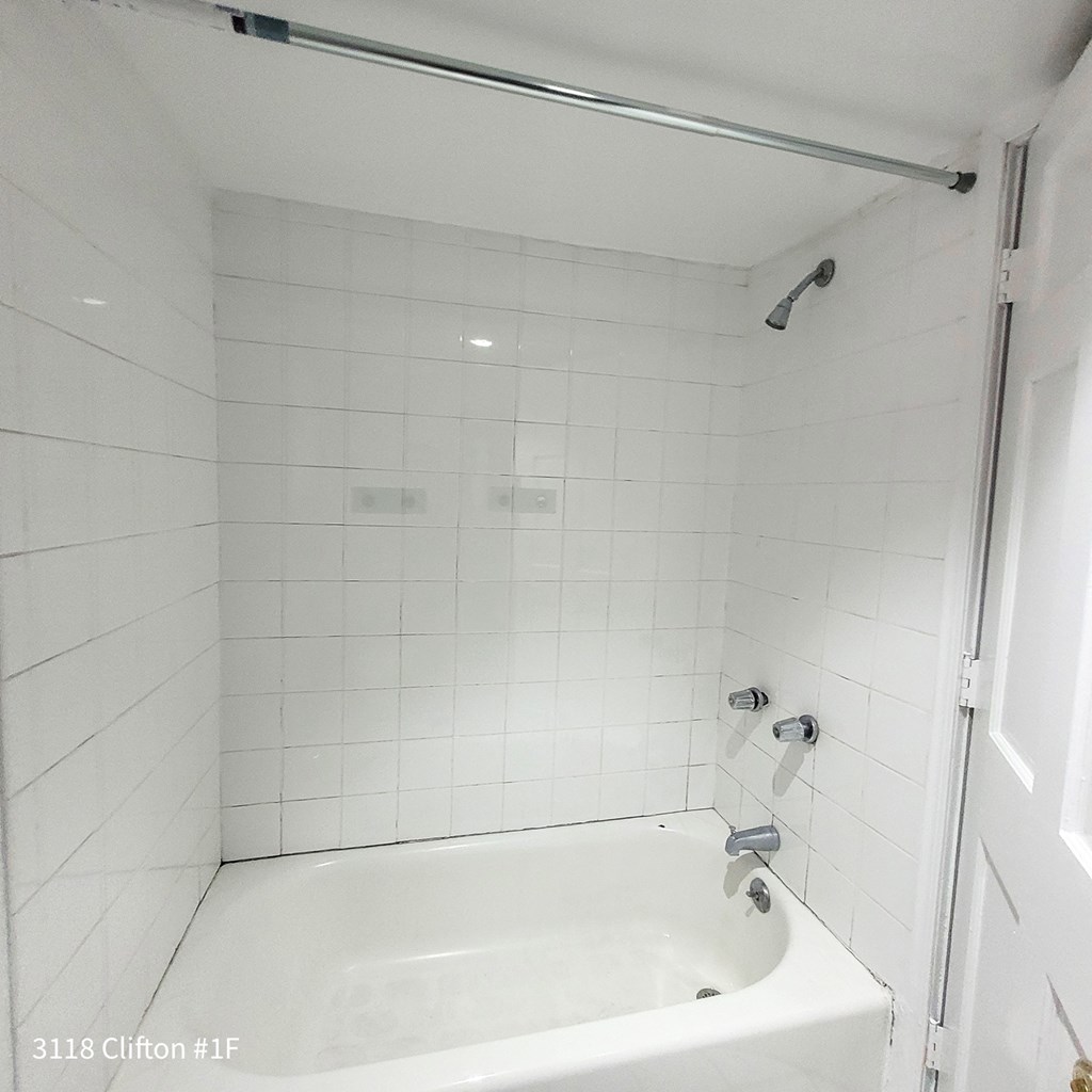 a white tiled bathroom with a tub and a shower
